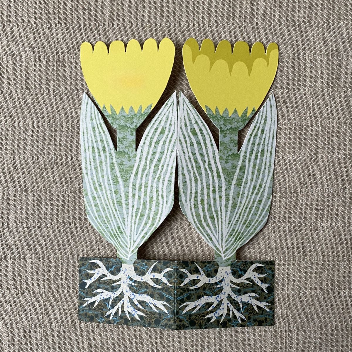Splayed yellow tulip shaped greetings card on a neutral background