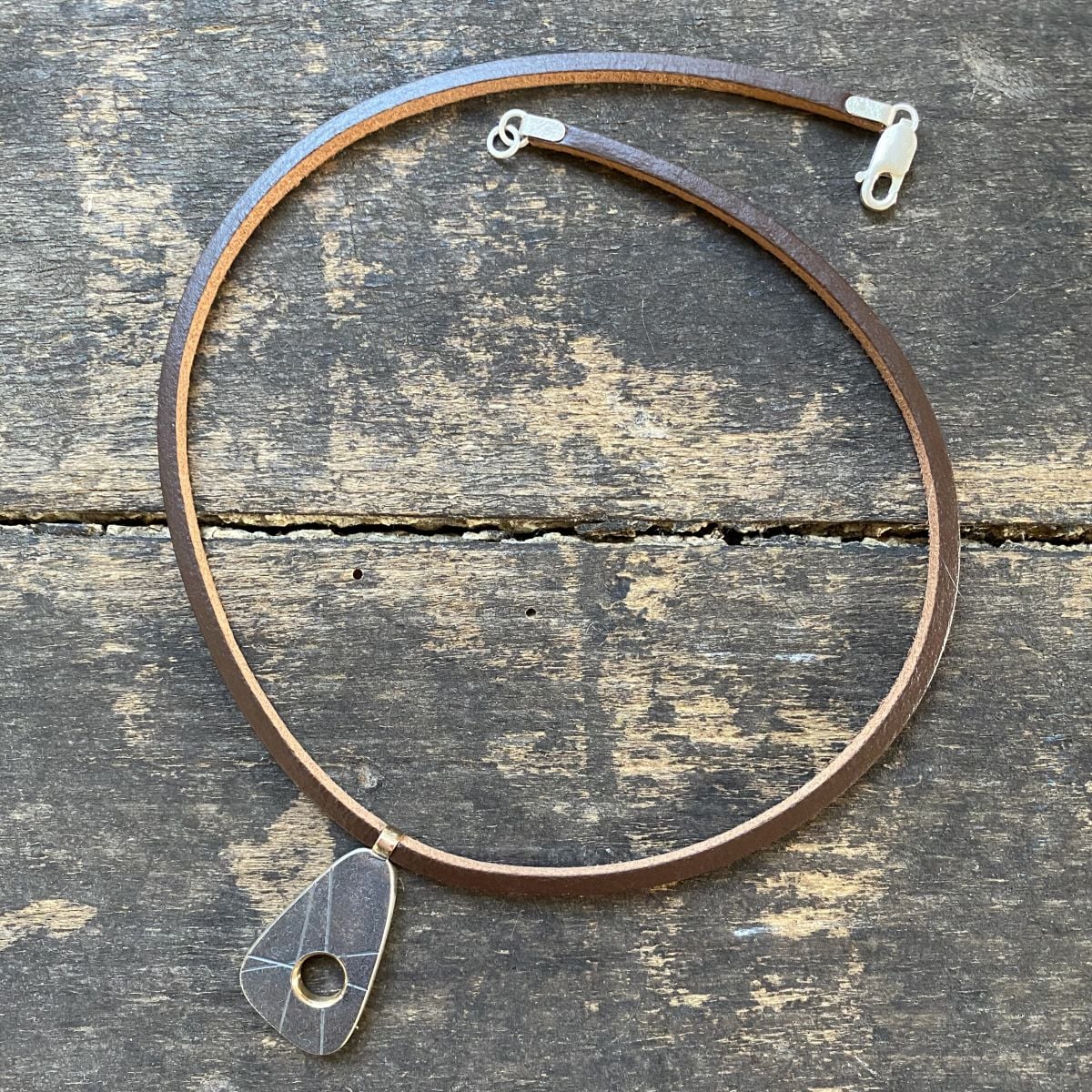 silver pendant on a leather thong necklace by Clare de la Torre on a wooden background