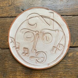 Round plate with letterpress blocks impressed into the clay to make a face. By John Ingledew.