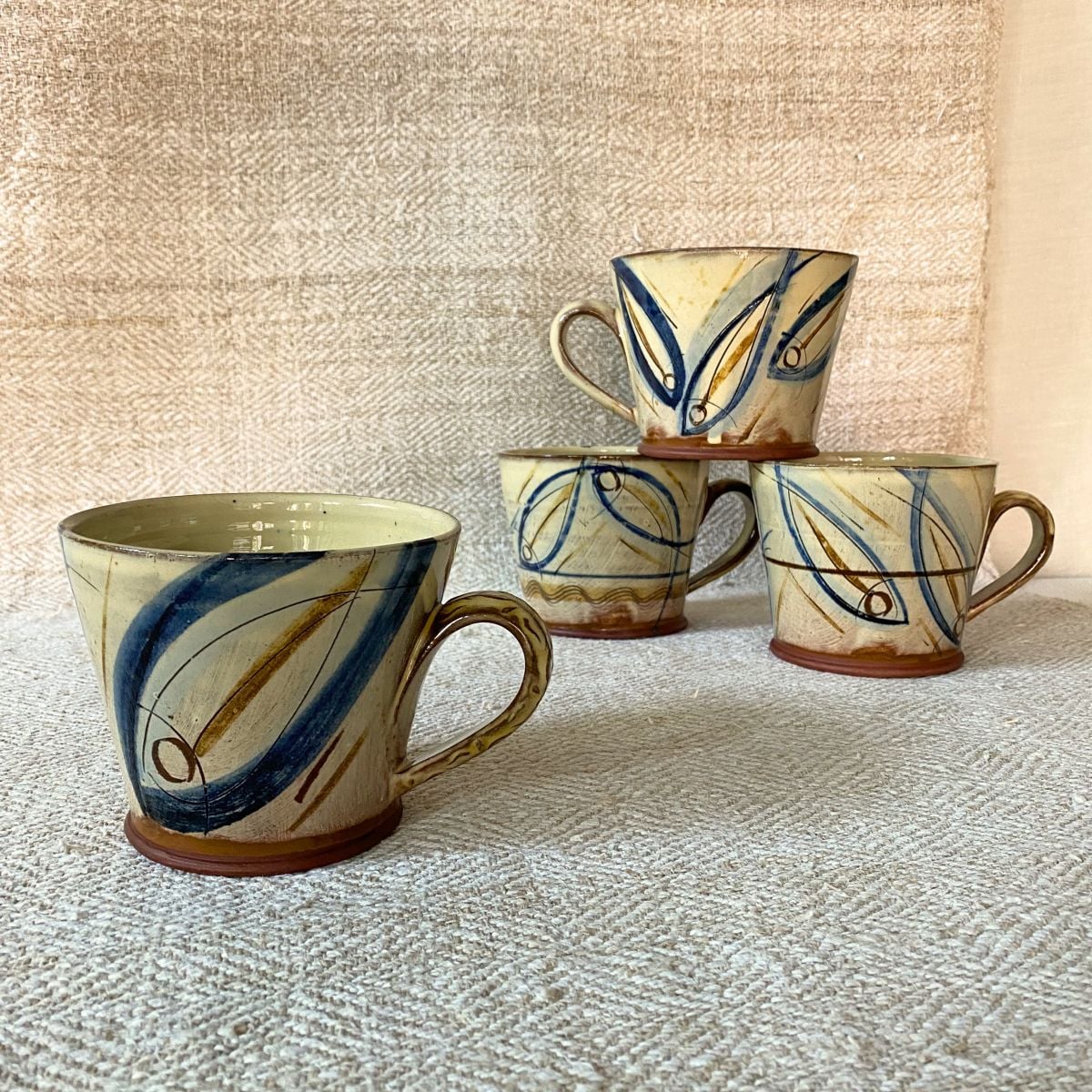 Jennifer Hall Stack of ceramic mugs on cream textile backdrop