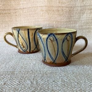 Jennifer Hall pair of slipware glazed tea mugs on a cream textile background