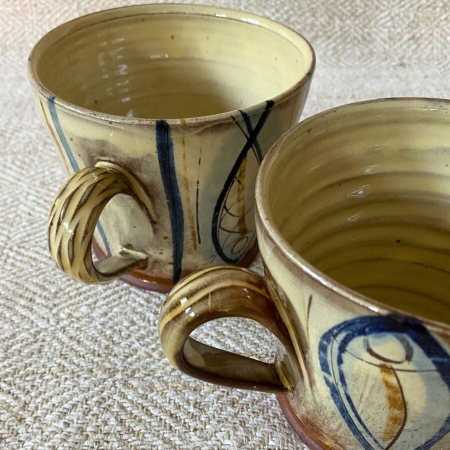 Jennifer Hall pair of slipware glazed tea mugs on a cream textile background