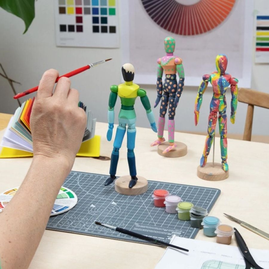 Three Paint & Pose Mannequins being painted in rainbow colours, posed on a table