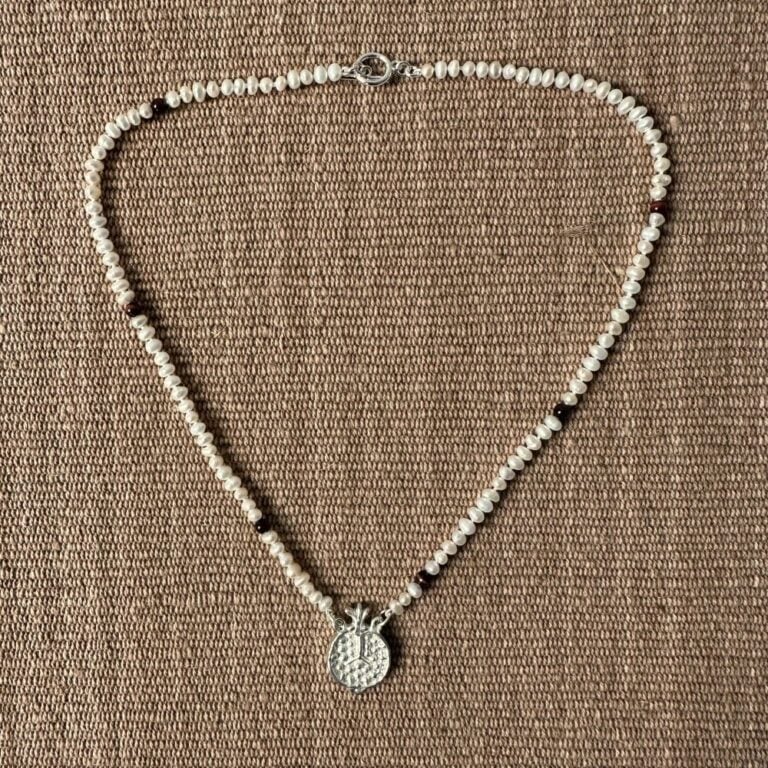 A seed pearl and red tigers eye necklace with a cast silver pomegranate pendant. Clare de la Torre.