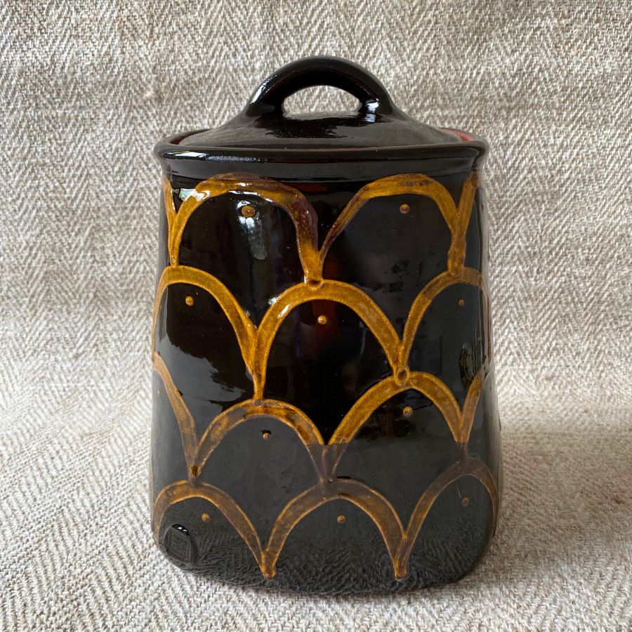 Black glazed jar with lid against a pale fabric backdrop.