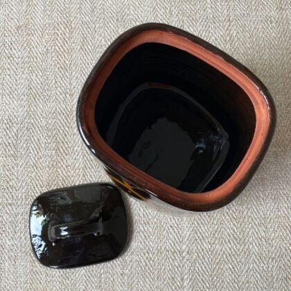Black glazed jar with lid against a pale fabric backdrop.