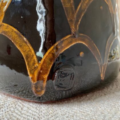 Black glazed jar with lid against a pale fabric backdrop.
