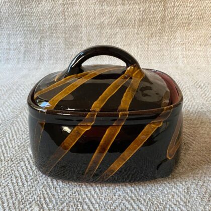 Black glazed butter dish with lid against a pale fabric backdrop.