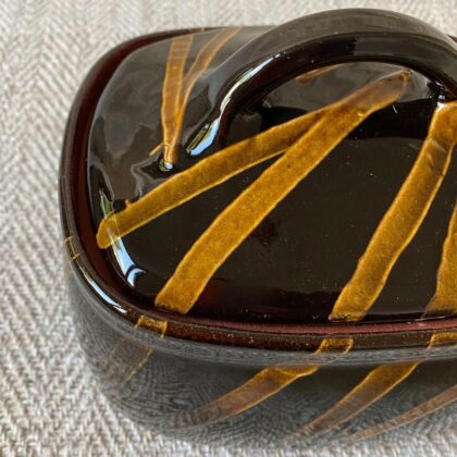 Black glazed butter dish with lid against a pale fabric backdrop.