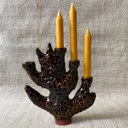 Black glazed candelabra with mottled decoration against a pale fabric backdrop.