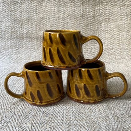 Trio of amber slipware mugs by Erica Taylor Low against a fabric background