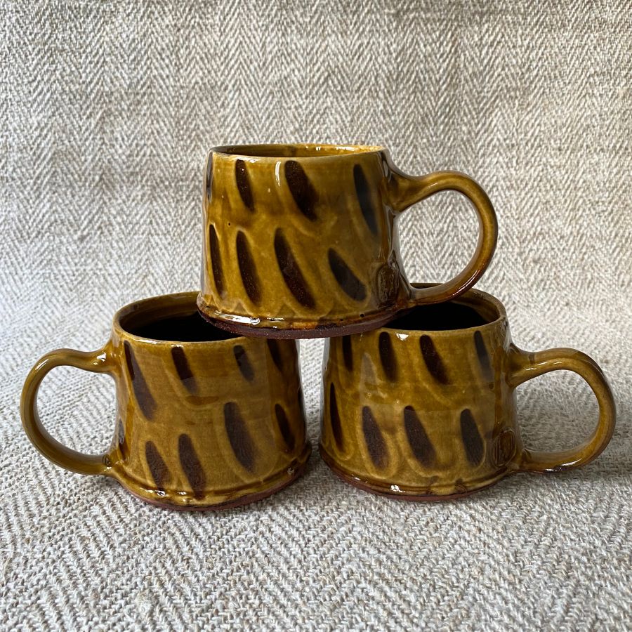 Trio of amber slipware mugs by Erica Taylor Low against a fabric background