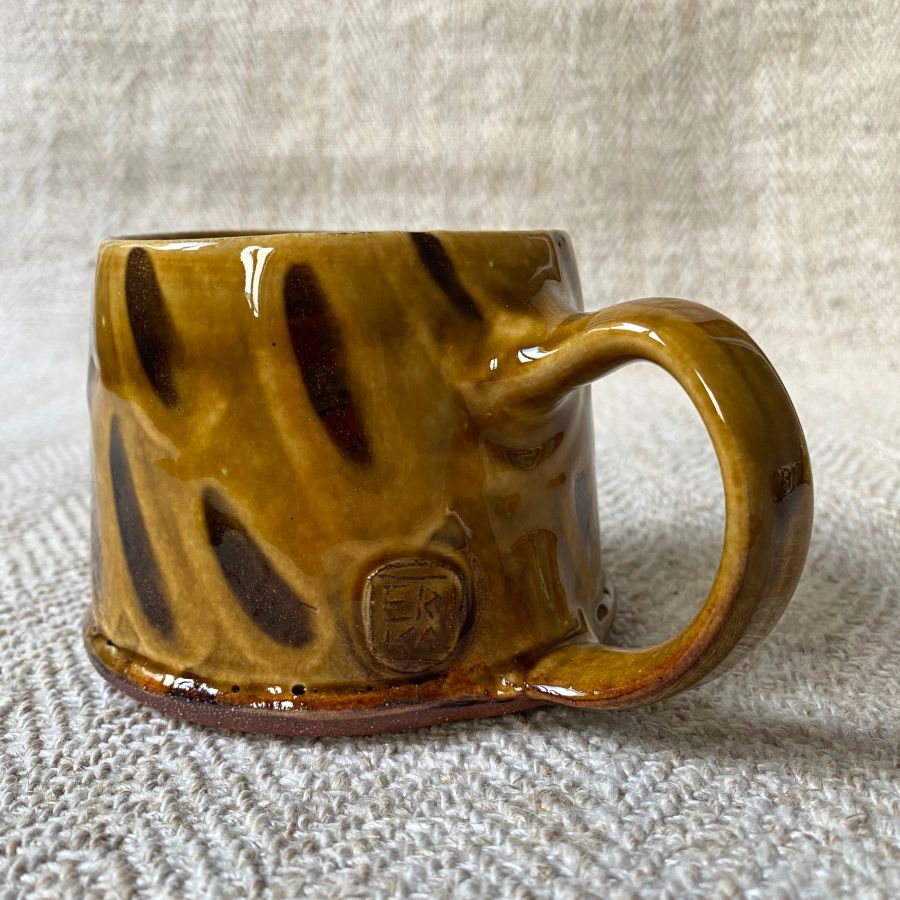 Trio of amber slipware mugs by Erica Taylor Low against a fabric background