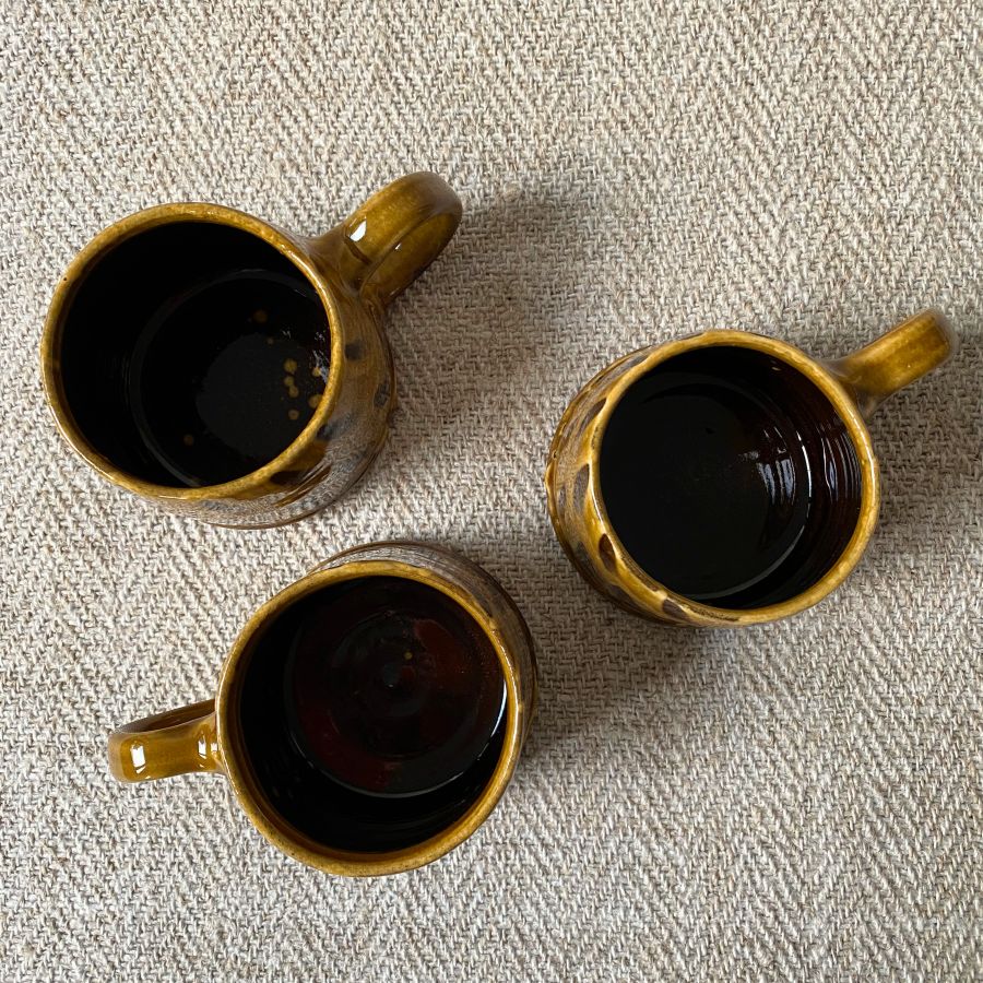 Trio of amber slipware mugs by Erica Taylor Low against a fabric background